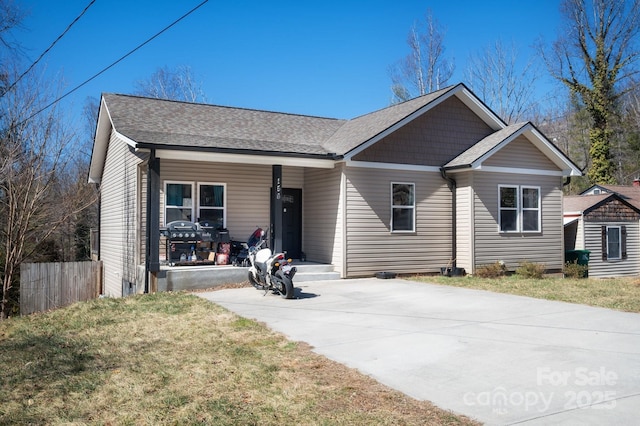 ranch-style house featuring roof with shingles, a front yard, and fence