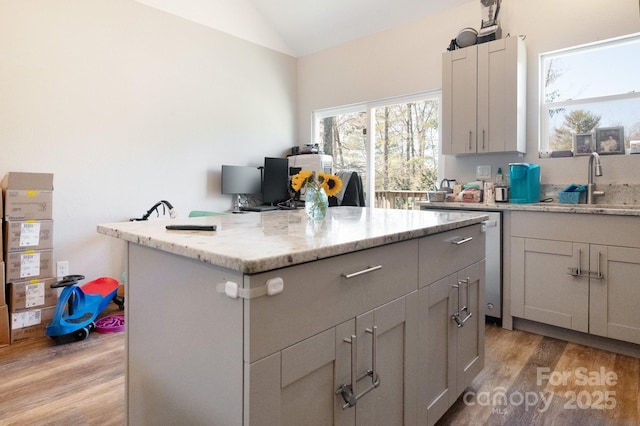 kitchen featuring light stone counters, a center island, light wood finished floors, a sink, and vaulted ceiling