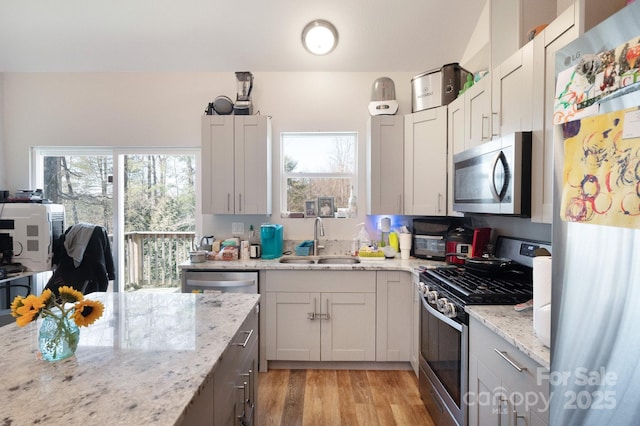 kitchen with stainless steel appliances, plenty of natural light, a sink, and light stone countertops