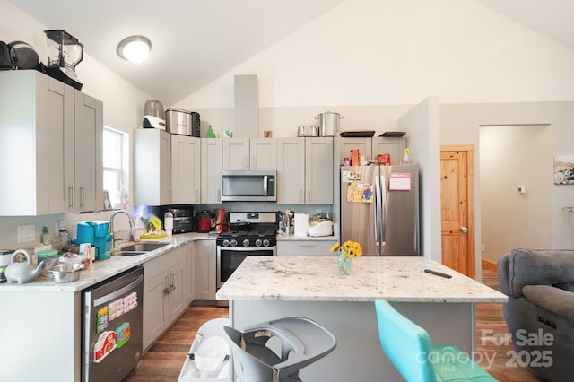 kitchen featuring appliances with stainless steel finishes, a breakfast bar, light stone countertops, vaulted ceiling, and a sink