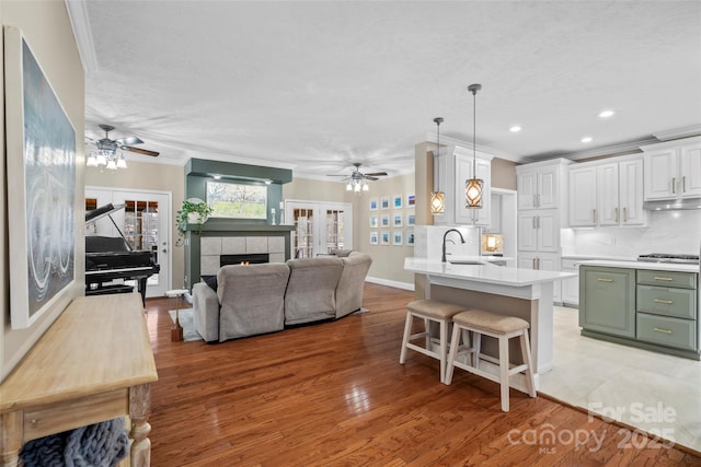 kitchen with ornamental molding, green cabinetry, under cabinet range hood, and a kitchen bar