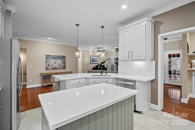 kitchen featuring light wood finished floors, ornamental molding, a peninsula, stainless steel appliances, and a sink