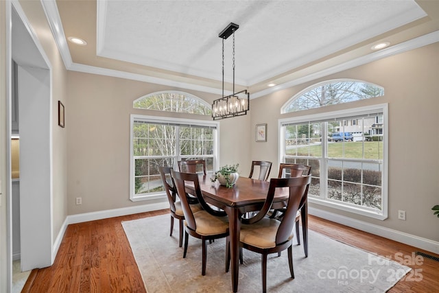 dining area with baseboards, visible vents, a tray ceiling, and wood finished floors