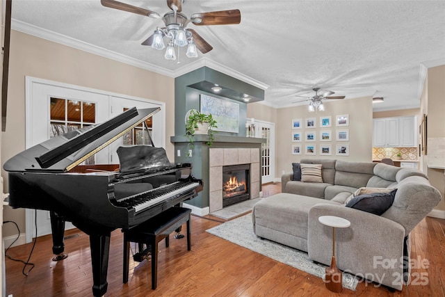 living room featuring crown molding, a fireplace, ceiling fan, a textured ceiling, and light wood-type flooring