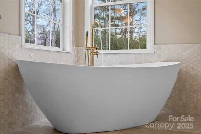 full bath with a soaking tub, wainscoting, and tile walls