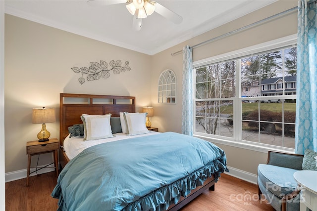 bedroom with crown molding, multiple windows, baseboards, and wood finished floors