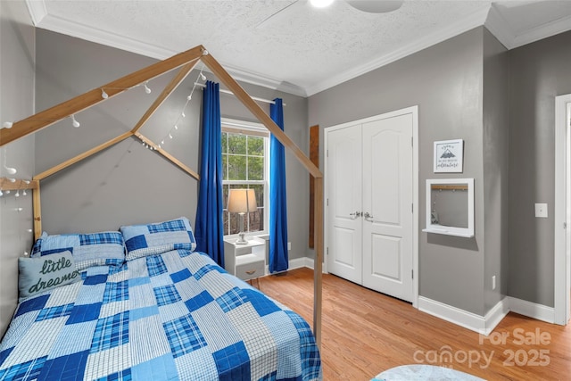 bedroom featuring a textured ceiling, wood finished floors, baseboards, ornamental molding, and a closet