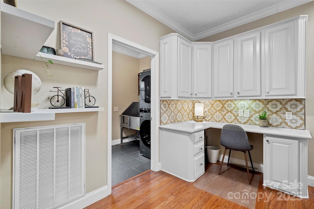 office space featuring stacked washer and dryer, baseboards, light wood-style floors, built in desk, and crown molding