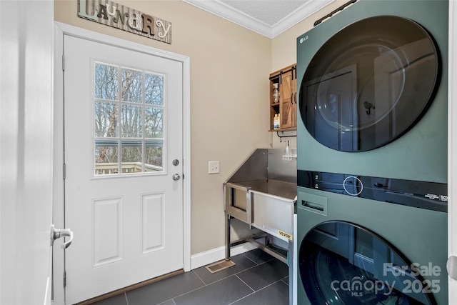 laundry area with stacked washer and clothes dryer, crown molding, laundry area, dark tile patterned floors, and baseboards