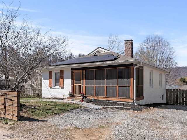 view of front of house with fence, brick siding, solar panels, and a sunroom