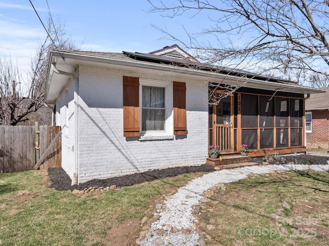 bungalow-style home with brick siding, fence, a front yard, and a sunroom