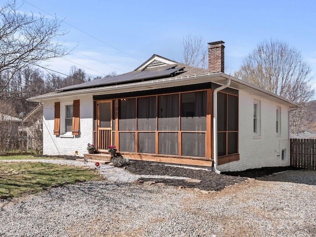 exterior space with fence, solar panels, a sunroom, a chimney, and brick siding