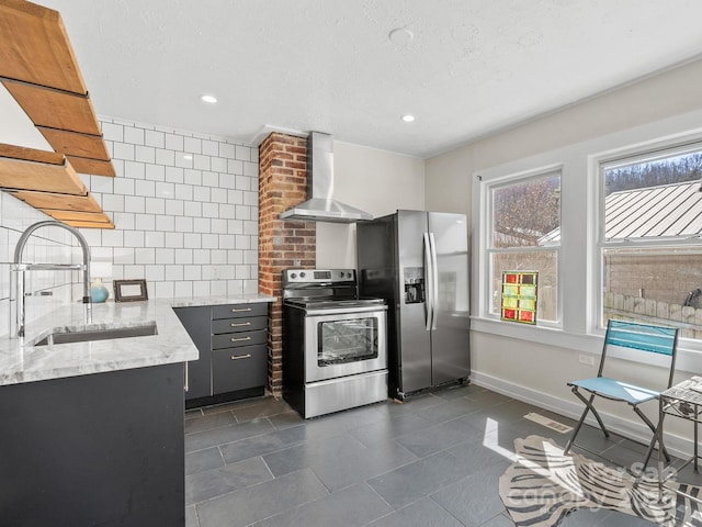 kitchen with backsplash, light stone counters, appliances with stainless steel finishes, wall chimney exhaust hood, and a sink