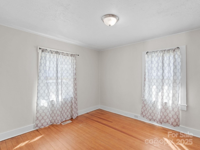 spare room with visible vents, a textured ceiling, baseboards, and wood finished floors