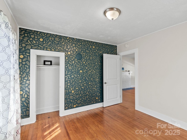 unfurnished bedroom featuring a closet, wallpapered walls, baseboards, and wood finished floors