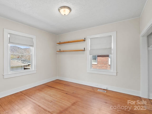 spare room with visible vents, a textured ceiling, light wood-type flooring, and baseboards