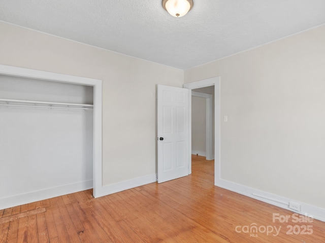 unfurnished bedroom featuring a closet, light wood-style flooring, a textured ceiling, and baseboards