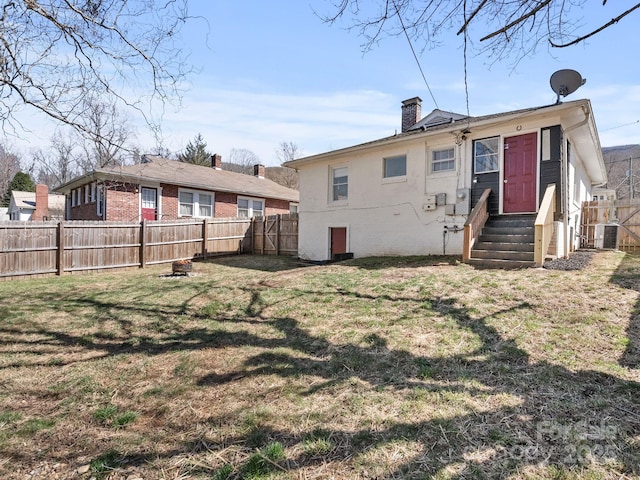 rear view of house featuring brick siding, entry steps, a lawn, a chimney, and a fenced backyard