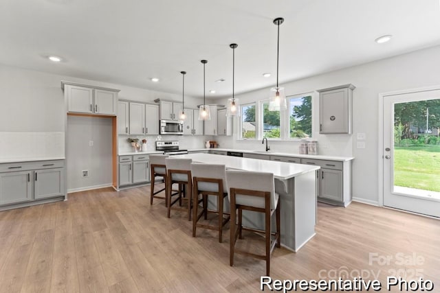 kitchen with a center island, decorative light fixtures, light countertops, appliances with stainless steel finishes, and a sink