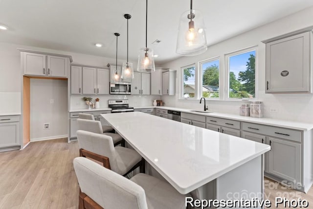 kitchen with a sink, light countertops, appliances with stainless steel finishes, hanging light fixtures, and a center island