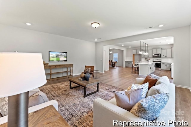 living area featuring light wood finished floors, recessed lighting, baseboards, and an inviting chandelier