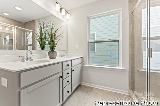 full bath with double vanity, a shower stall, baseboards, and a sink