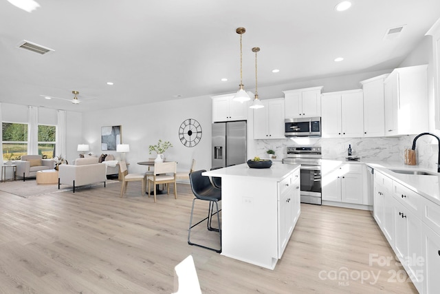 kitchen with stainless steel appliances, light countertops, decorative backsplash, a sink, and a kitchen island