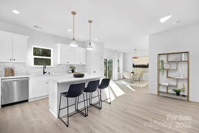 kitchen featuring tasteful backsplash, light countertops, visible vents, a sink, and dishwasher