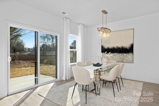 dining space with an inviting chandelier, baseboards, visible vents, and wood finished floors