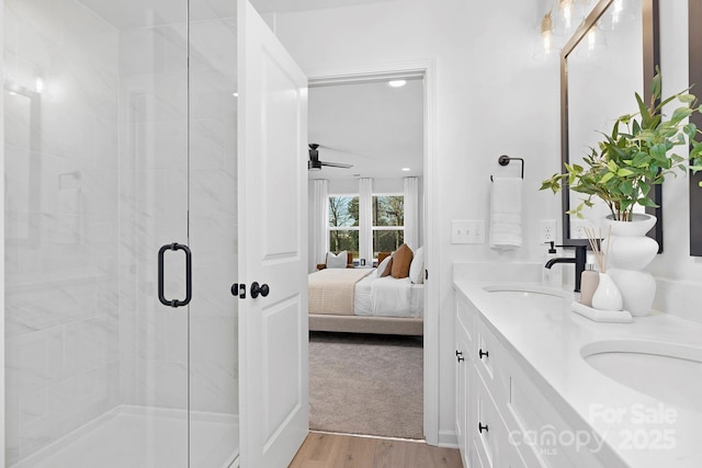 ensuite bathroom featuring ensuite bathroom, wood finished floors, a sink, double vanity, and a stall shower