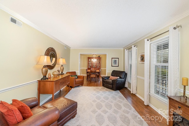 living area with visible vents, baseboards, wood finished floors, and ornamental molding