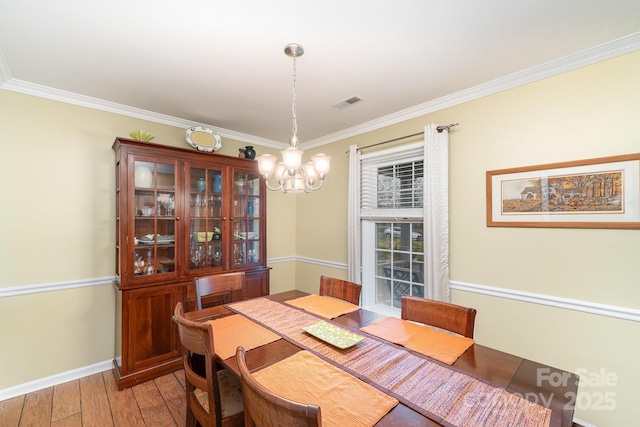 dining area with visible vents, light wood-style flooring, ornamental molding, an inviting chandelier, and baseboards