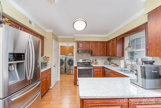 kitchen featuring washing machine and clothes dryer, a sink, stainless steel appliances, light wood-style floors, and tasteful backsplash