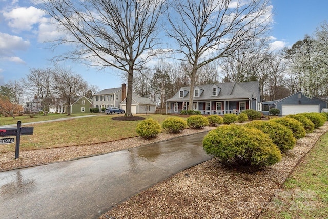 new england style home with a garage, a porch, an outdoor structure, and a front lawn