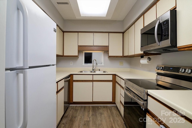 kitchen with stainless steel appliances, light countertops, a sink, and wood finished floors