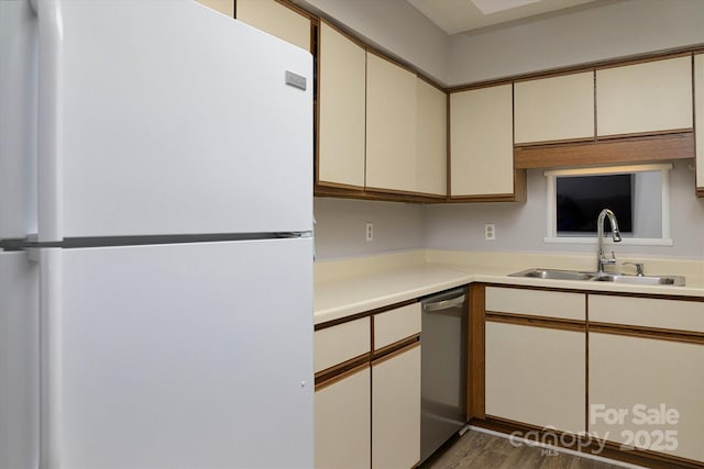 kitchen featuring freestanding refrigerator, a sink, light countertops, cream cabinetry, and stainless steel dishwasher