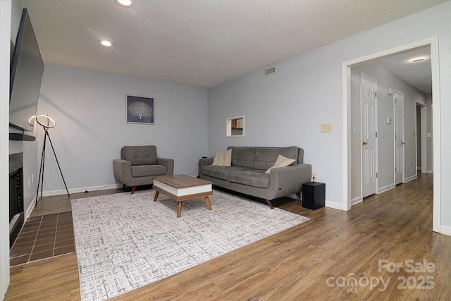 living area featuring a fireplace with flush hearth, visible vents, baseboards, and wood finished floors