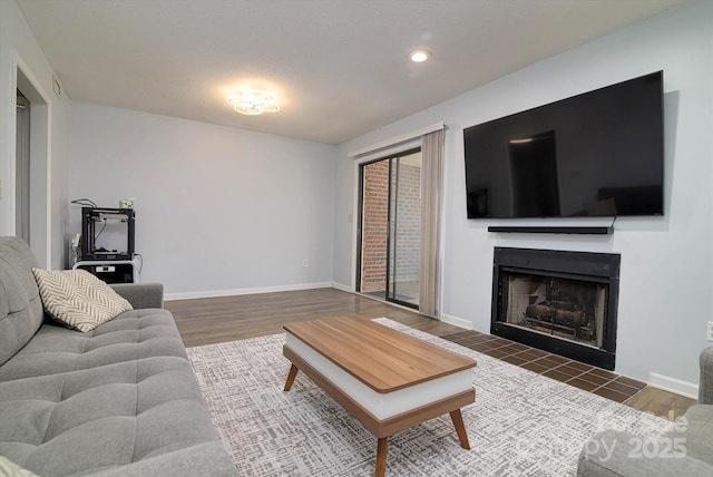 living room featuring recessed lighting, a fireplace with raised hearth, baseboards, and wood finished floors