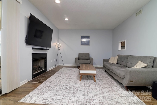 living room featuring recessed lighting, a fireplace with flush hearth, wood finished floors, baseboards, and visible vents