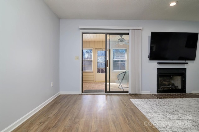 unfurnished living room featuring a fireplace with flush hearth, baseboards, and wood finished floors