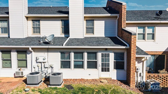 back of property with roof with shingles, a chimney, and cooling unit