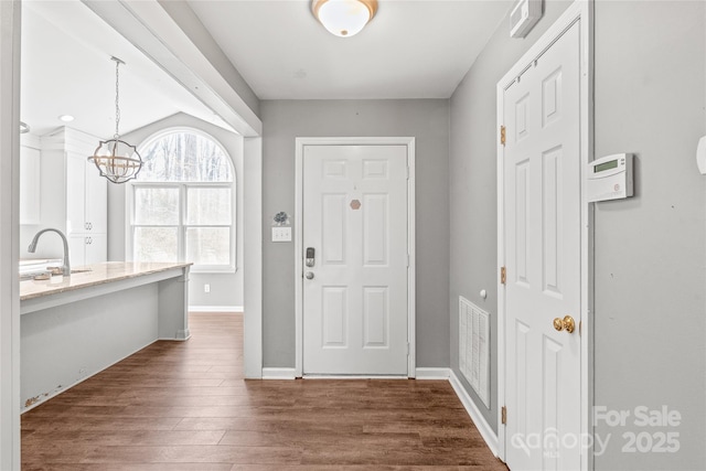 foyer entrance featuring a chandelier, visible vents, dark wood finished floors, and baseboards