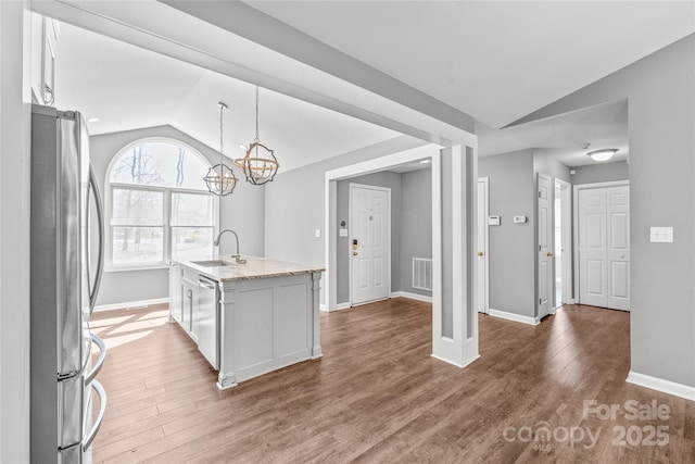 kitchen featuring vaulted ceiling, stainless steel appliances, a sink, and wood finished floors