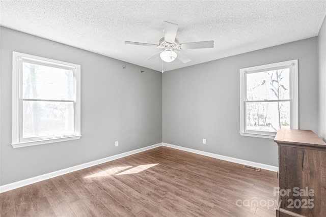 unfurnished room featuring baseboards, wood finished floors, visible vents, and a healthy amount of sunlight