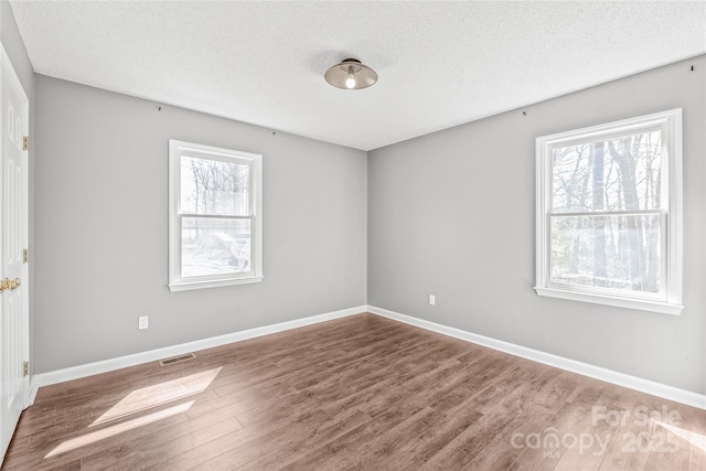 empty room with a healthy amount of sunlight, visible vents, a textured ceiling, and wood finished floors