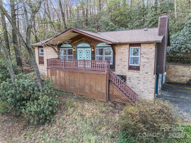 ranch-style home with stairs, brick siding, roof with shingles, and a chimney