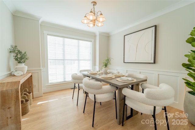 dining room featuring light wood-type flooring, an inviting chandelier, a decorative wall, and crown molding