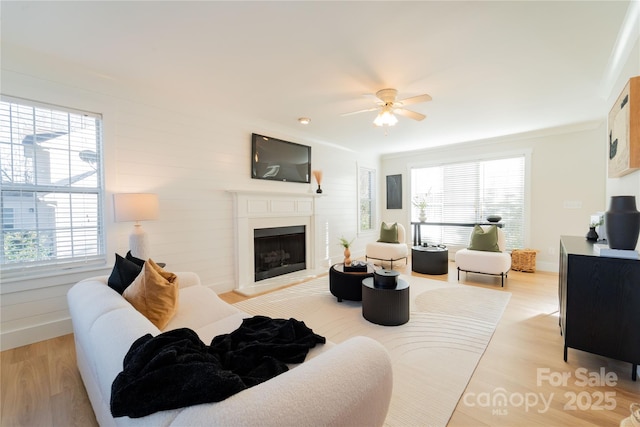 living area featuring a ceiling fan, baseboards, a fireplace with raised hearth, and light wood finished floors