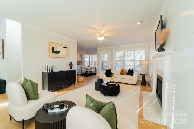 living room featuring a fireplace with flush hearth, ceiling fan, crown molding, and wood finished floors