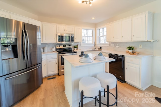 kitchen with stainless steel appliances, visible vents, light wood-style flooring, white cabinetry, and a sink